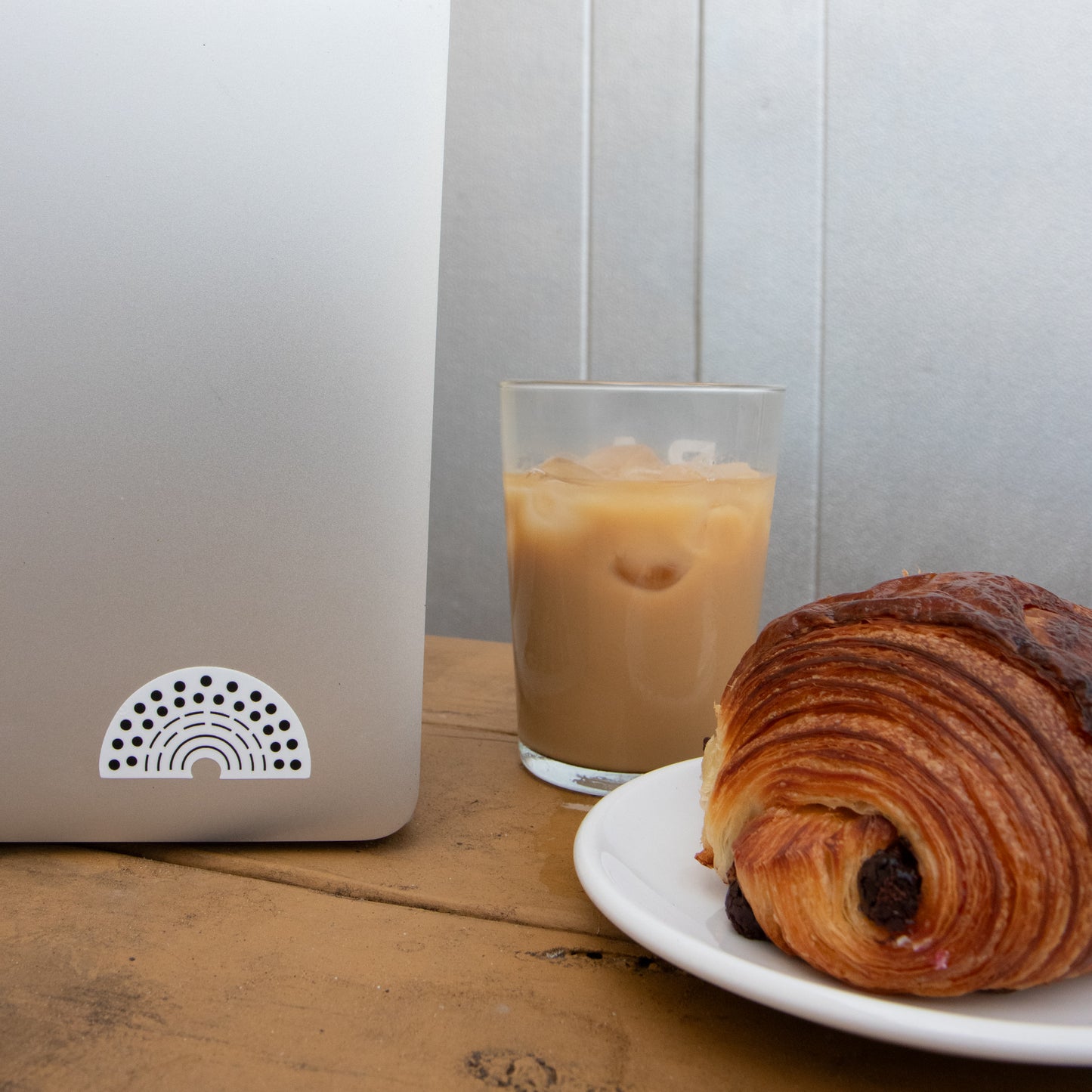 Laptop with a multicolored pride sticker amidst a coffee and croissant