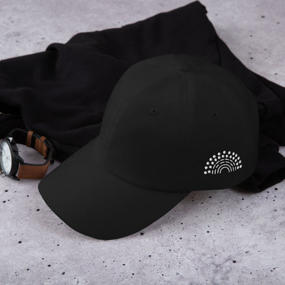 black baseball dad hat with white pride rainbow embroidered on the left of the hat amongst other clothing items