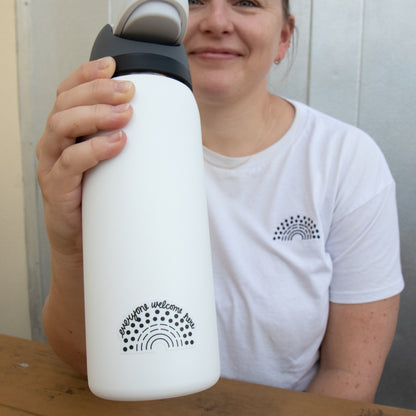 Person holding a water bottle with a black pride sticker with the phrase everyone welcome here