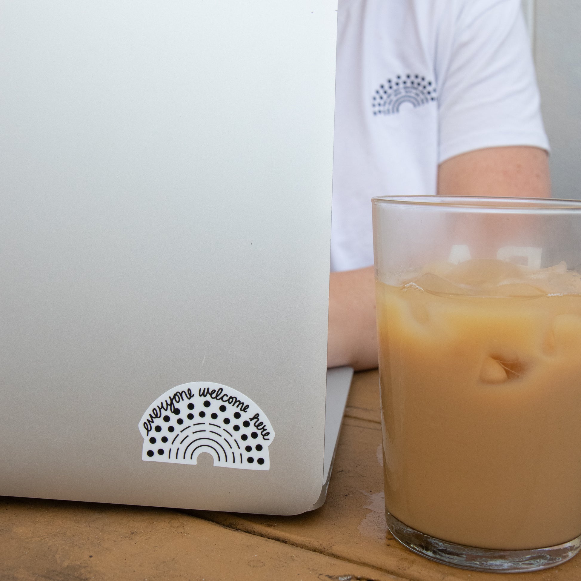 Zoomed in image of a laptop with a black pride sticker with the phrase everyone welcome here