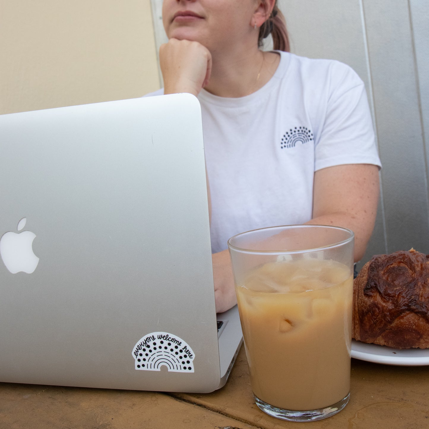 Person working on a laptop with a black pride sticker with the phrase everyone welcome here