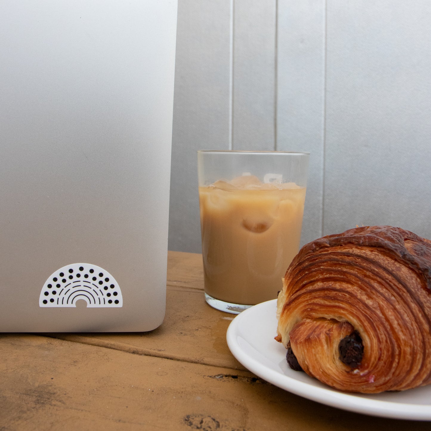 Laptop with a multicolored pride sticker amidst a coffee and croissant