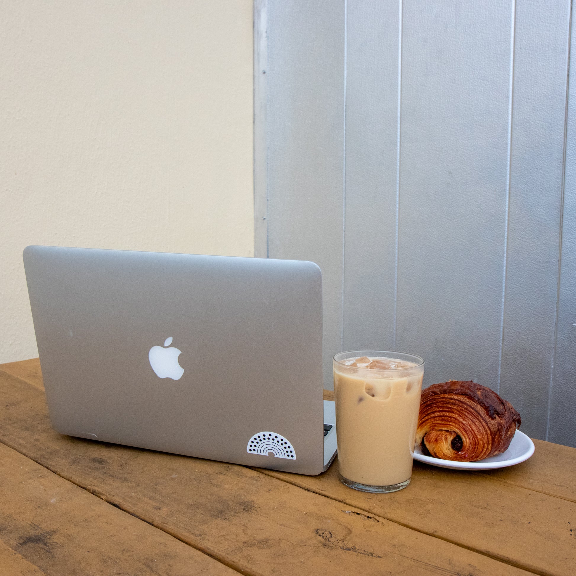 Laptop with a multicolored pride sticker amidst a coffee and croissant