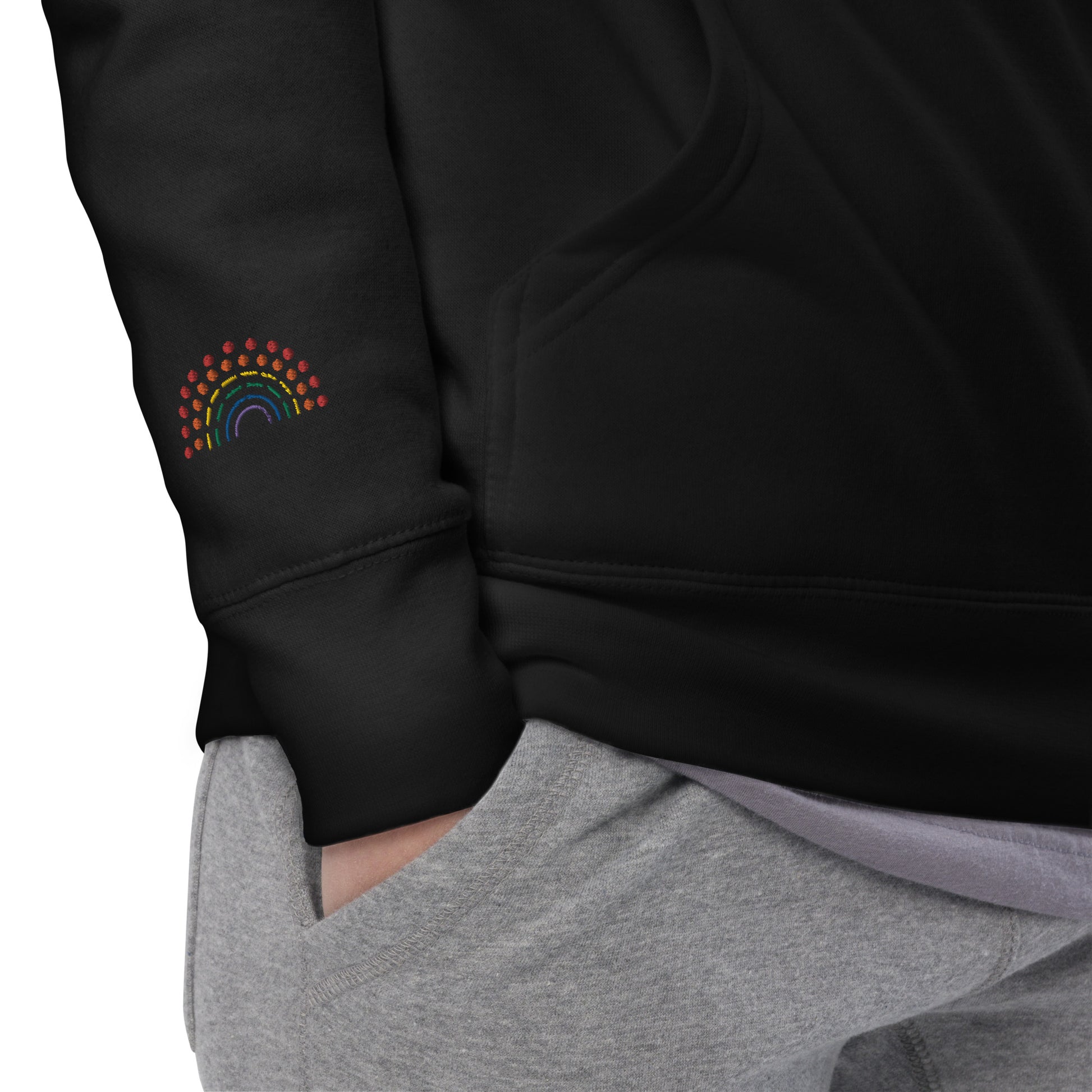 zoomed in image of person wearing a black crewneck sweatshirt with multicolored pride rainbow embroidered on the right wrist