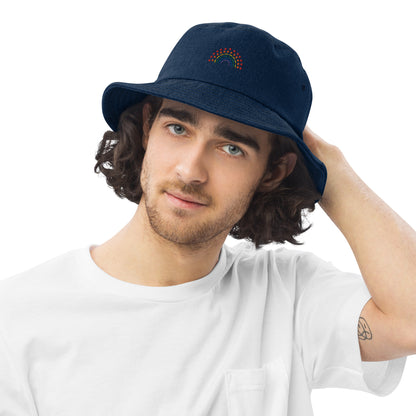 person wearing a dark blue denim bucket hat with multicolored pride rainbow embroidered on center of the hat