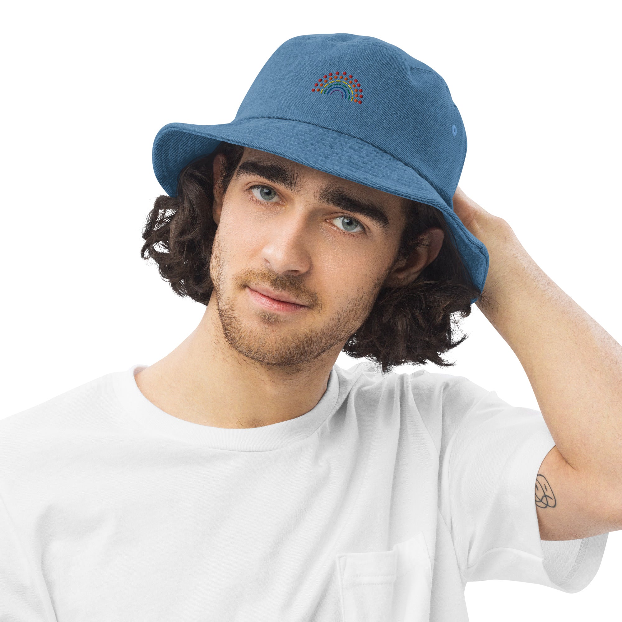 person wearing a light blue denim bucket hat with multicolored pride rainbow embroidered on center of the hat