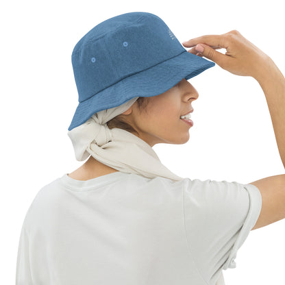 person wearing a light blue denim bucket hat with white pride rainbow embroidered on center of the hat