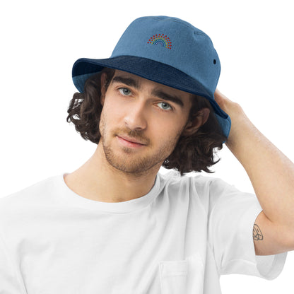 person wearing a mixed denim bucket hat with multicolored pride rainbow embroidered on center of the hat