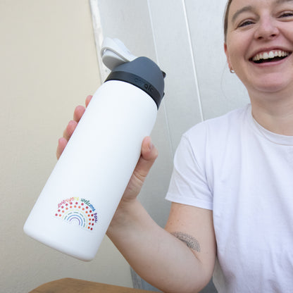 Person holding a water bottle with a multicolored pride sticker with the phrase everyone welcome here