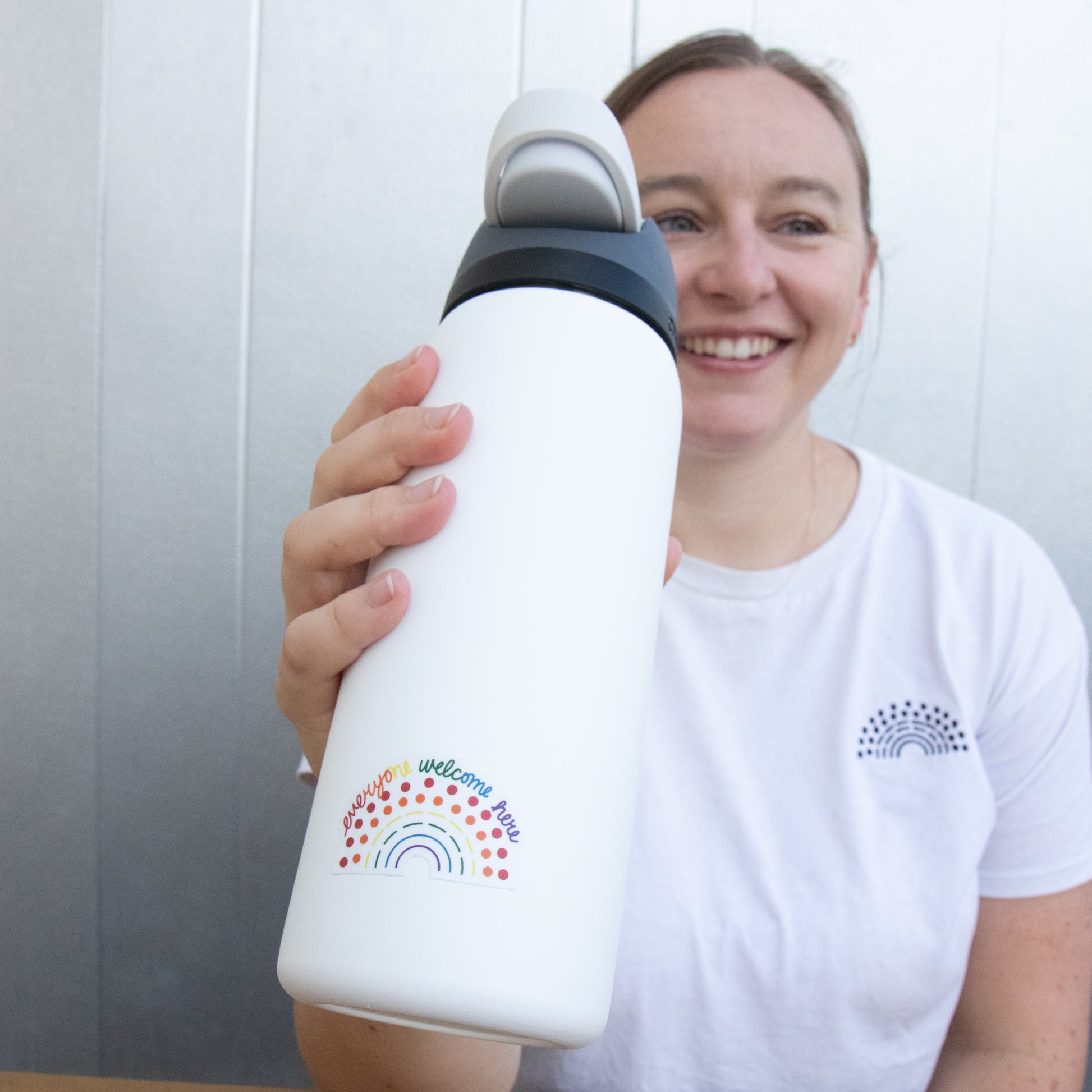 Person holding a water bottle with a multicolored pride sticker with the phrase everyone welcome here