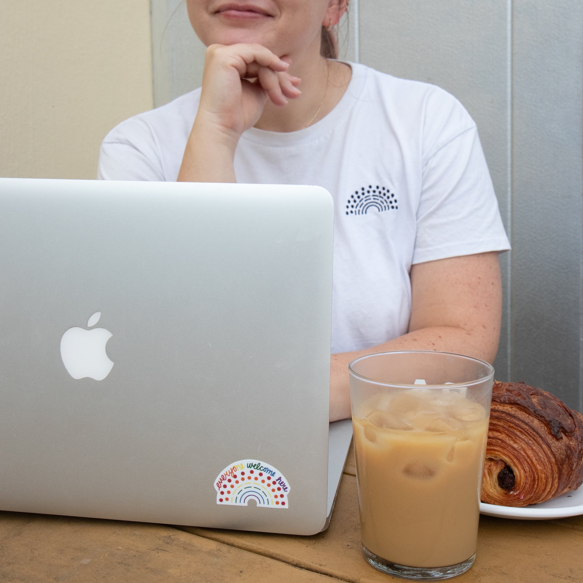 Person working on a laptop with a multicolored pride sticker with the phrase everyone welcome here