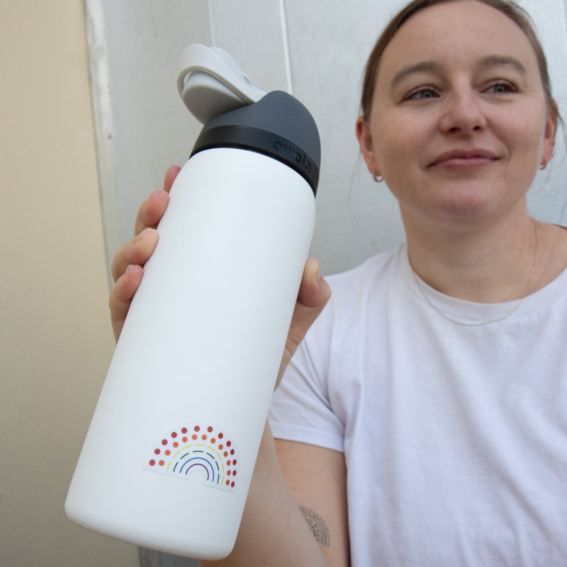 Person holding a water bottle with a multicolored pride sticker