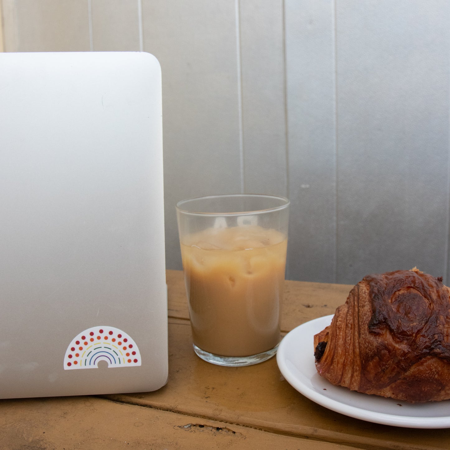 Laptop with a multicolored pride sticker  amidst a coffee and croissant