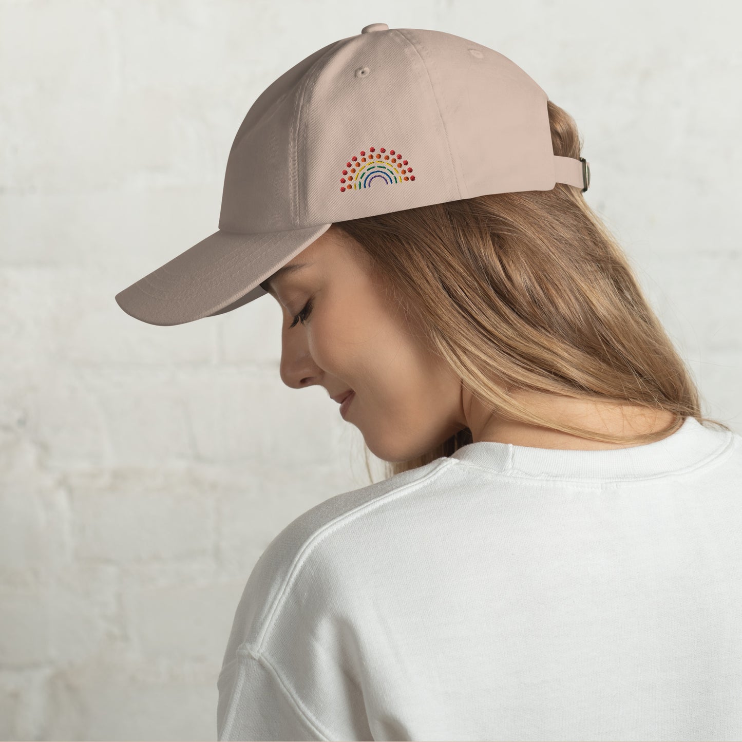 person wearing a stone tan baseball dad hat with multicolored pride rainbow embroidered on the left of the hat