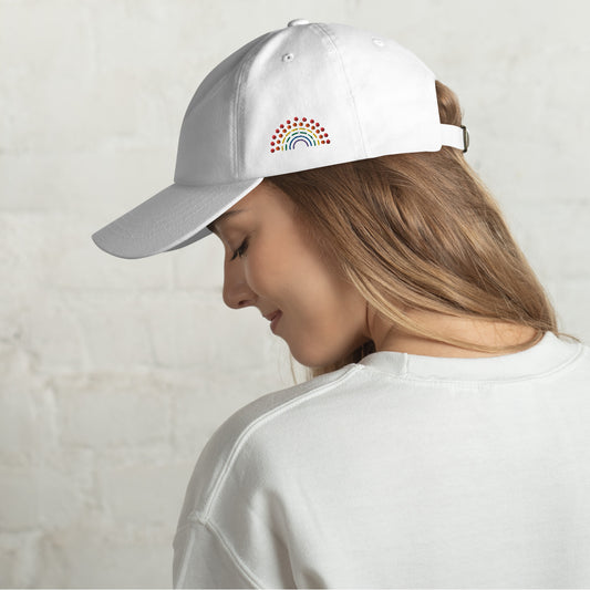 person wearing a white baseball dad hat with multicolored pride rainbow embroidered on the left of the hat