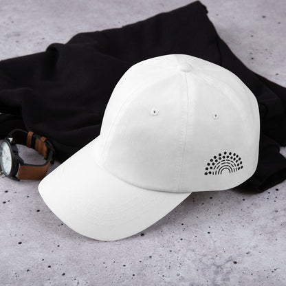 white baseball dad hat with black pride rainbow embroidered on the left of the hat amongst other clothing items